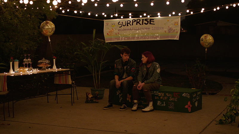 Two people sitting under a "surprise" sign.