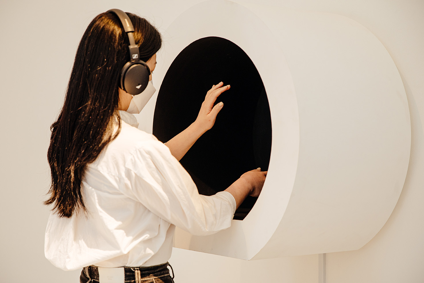 Person with headphones reaching arms into a round space in the wall