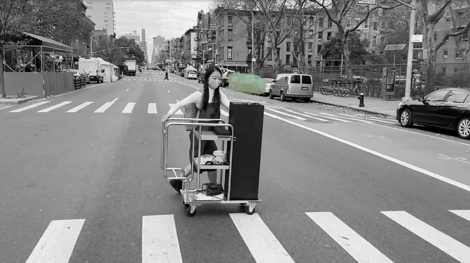 Woman rolling a cart with an invisible sculpture podium across the street