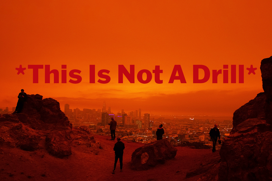an orange tinted image of people standing on a rock formation overlooking a city. The words: *This Is Not A Drill* are printed on top of the image