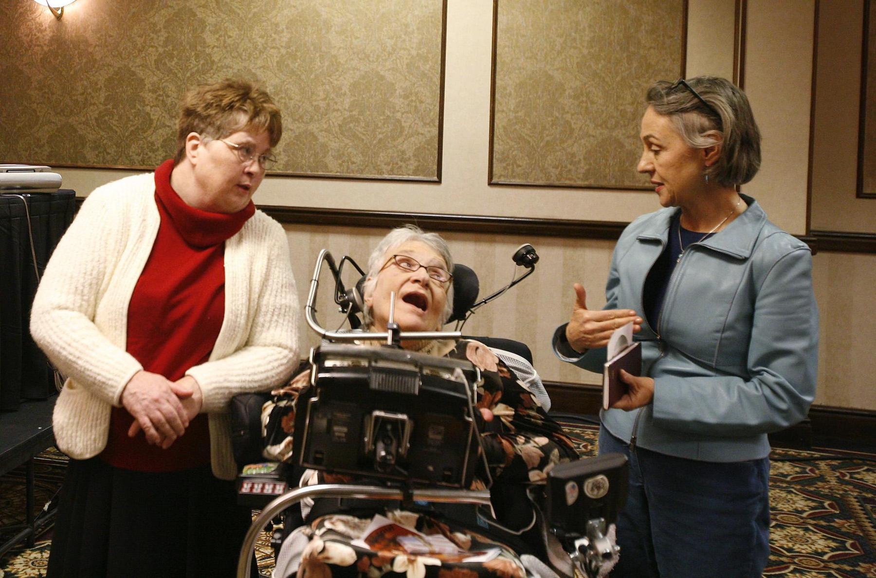 Three woman, one of whom is in a wheelchair, talk amongst themselves.