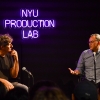 Filmmaker Jonathan Glazer sits with Grad Film Chair Andrew Okpeaha MacLean in front of a neon sign that reads "NYU Production Lab"