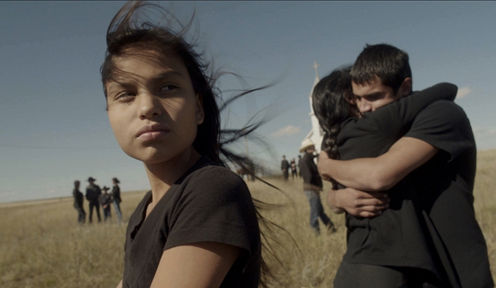 Film Still from My Brothers Taught Me, image of a young woman with a couple hugging in the background.