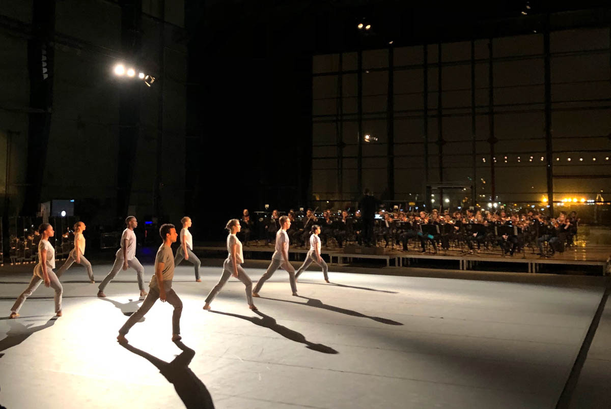 Dancers move in sync on stage while violinists play in the background