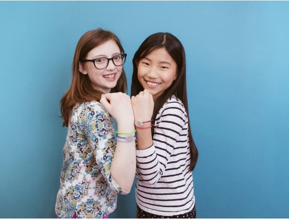 Two girls showing off their wearable Jewelbots on their wrists