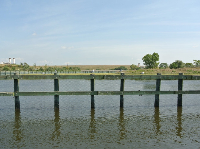 A landscape image of a wooden fence submerged in water against vast backdrop of grasslands