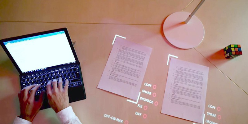A man typing something with a laptop with projected words around pieces of paper
