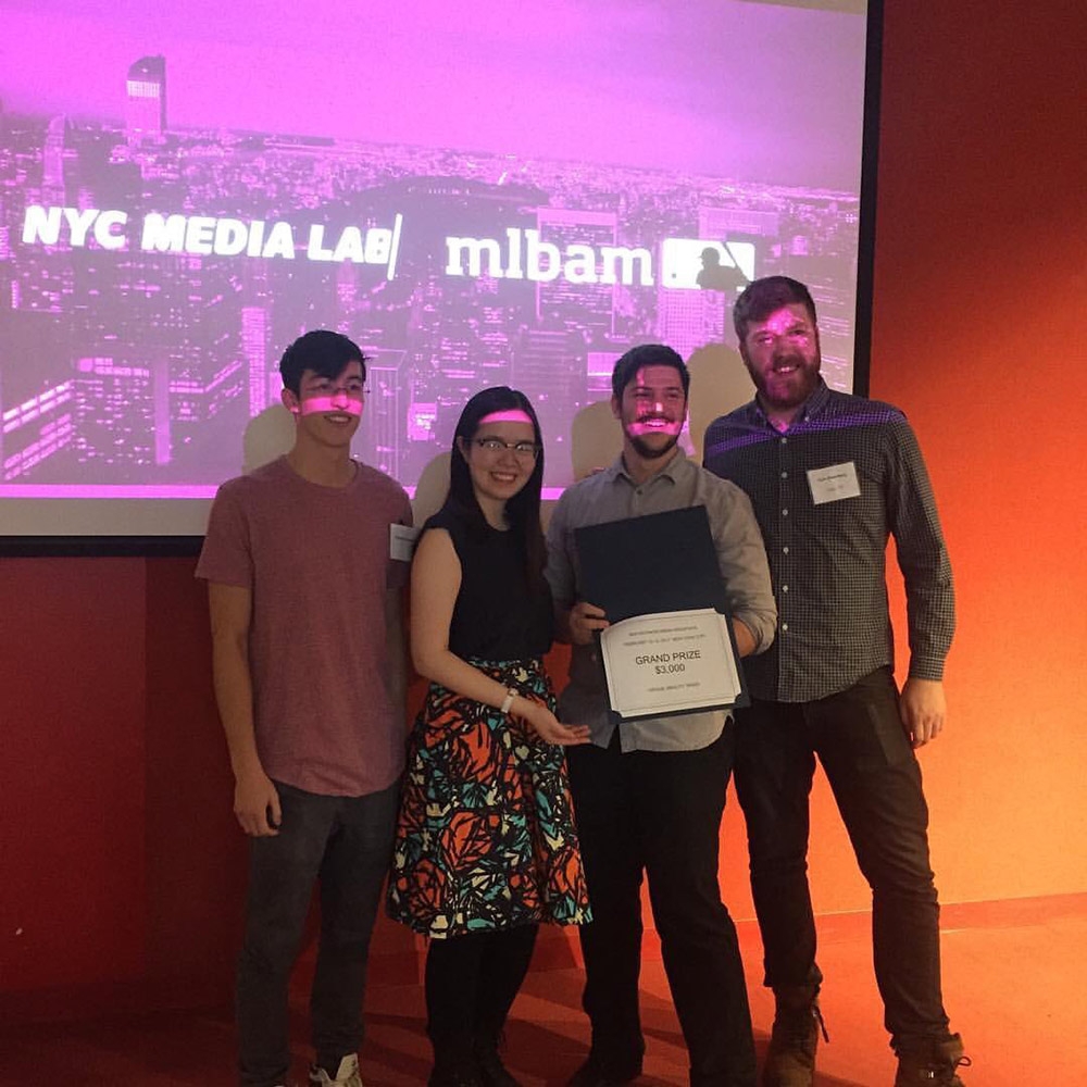 4 people smiling and showing an award with NYC Media Lab projected in the background