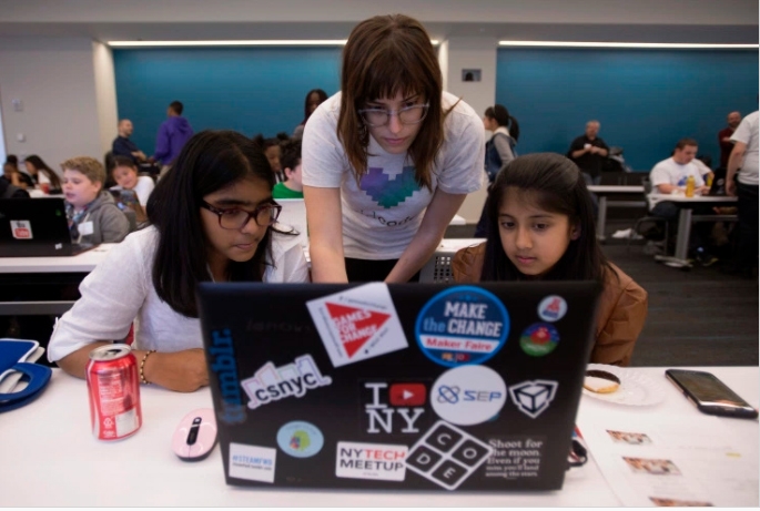 A woman standing over 2 students in front of a laptop