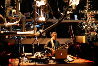 a wideshot of a person playing an eclectic guitar surrounded by other experimentally looking instruments