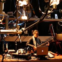 a wideshot of a person playing an eclectic guitar surrounded by other experimentally looking instruments