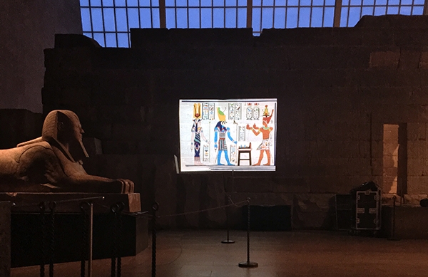 imagined drawings of Egyptian art projected on a wall next to a Sphinx statue