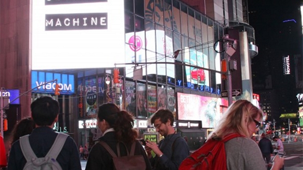 Times Square with the logo of Outrage Machine on display, with a few people looking at their cell phones