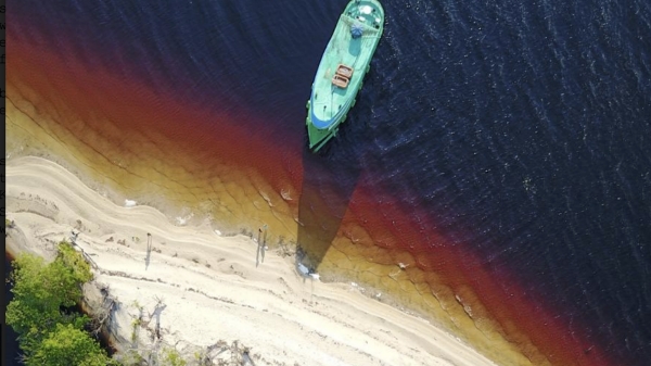 image of a blue boat approaching a dirty beach, taken from above