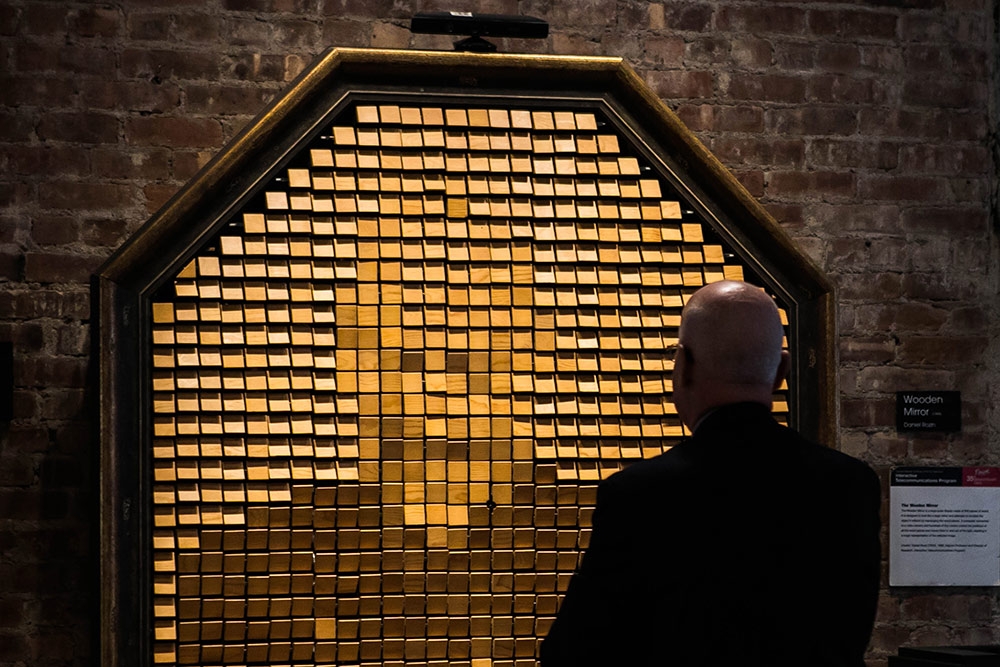 A wooden mirror that is reflecting a pixelated image of the man in front of it