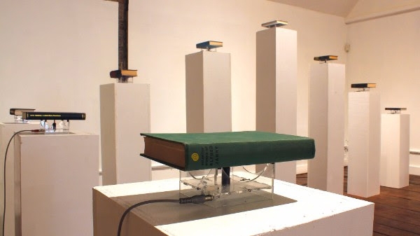A gallery exhibit of books hooked up to electronics and placed on pedestals