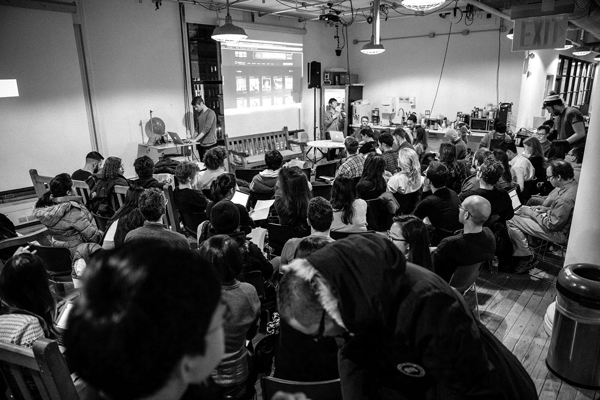 a person at a laptop in front of an audience filling the lounge