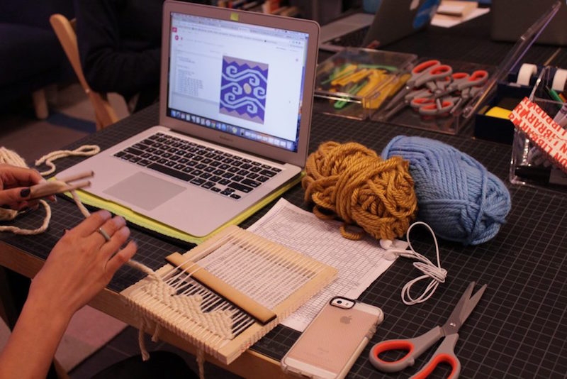 Person in front of computer with yarn and weaving instruments around