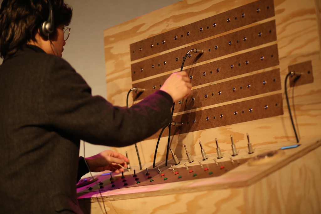 Image of Chino working on Operator, a large wooden control panel with switches and AUX cables coming in and out.