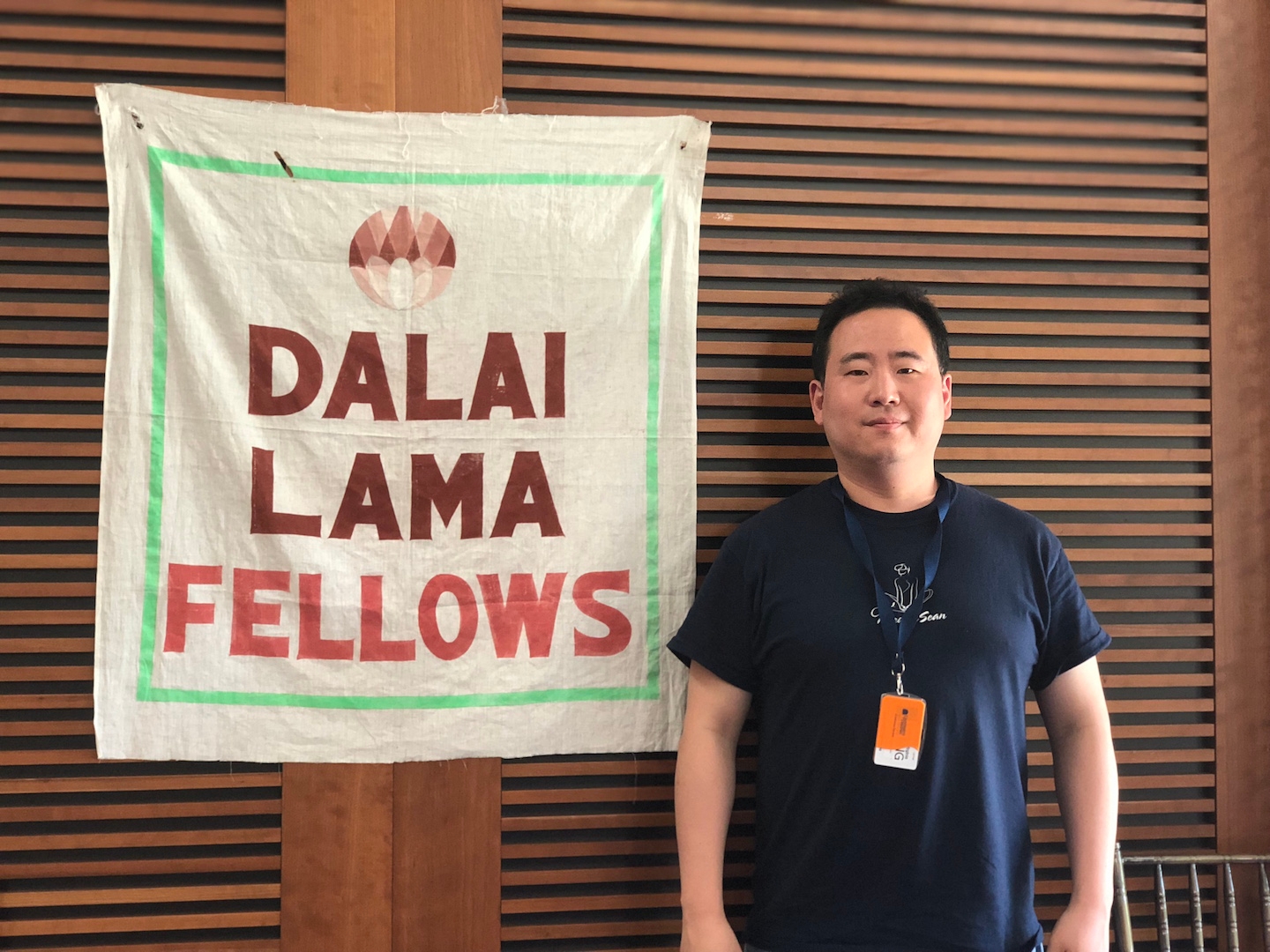 Image of Sean Kim in front of a poster that reads Dalai Lama Fellows at the Conference