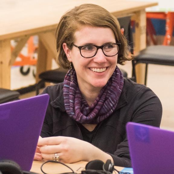 Image of woman with glasses on smiling while working on a computer.