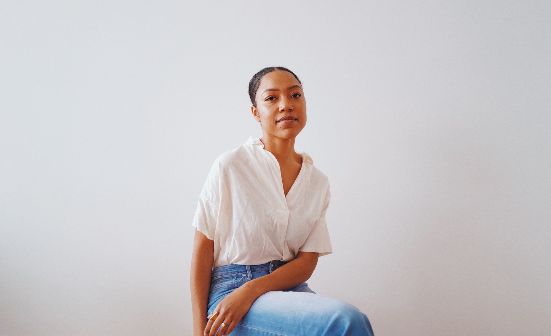 Image of woman wearing a white shirt sitting in front of a white and grey background.