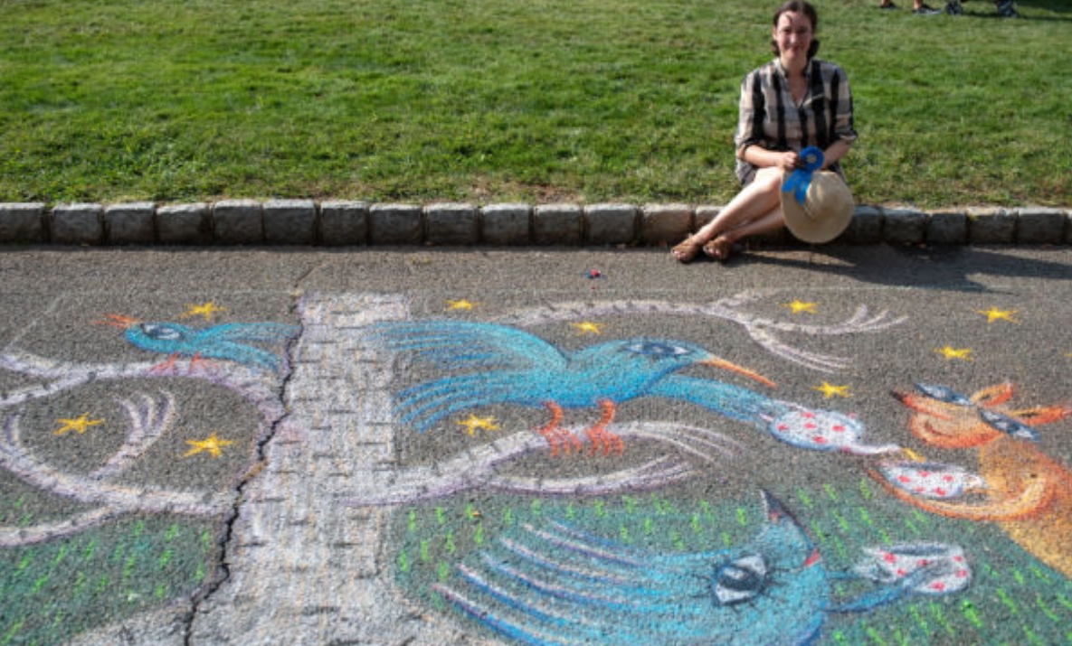 a woman sitting on the curb next to an intricate chalk drawing of a tree and bird