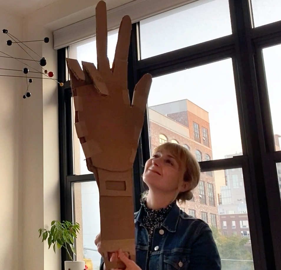 Image of woman standing next to giant cardboard hand.