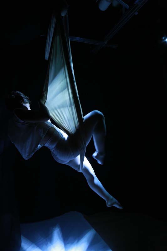 a silhouette of a woman on silk ropes with light reflecting
