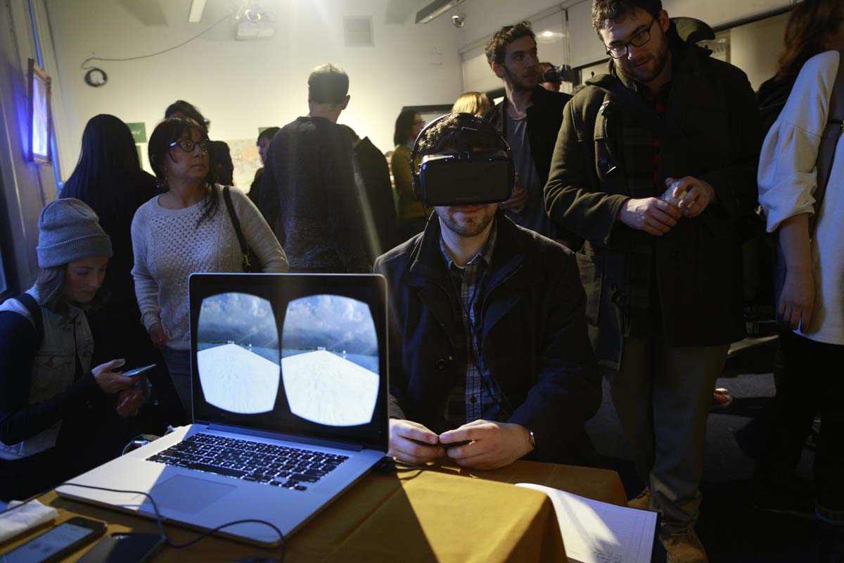 a person wearing VR goggles and the laptop that shows what he sees which is a barren landscape