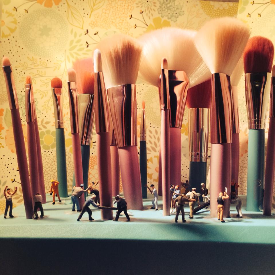 Fantastical image of miniature human figurines among seemingly giant makeup brushes