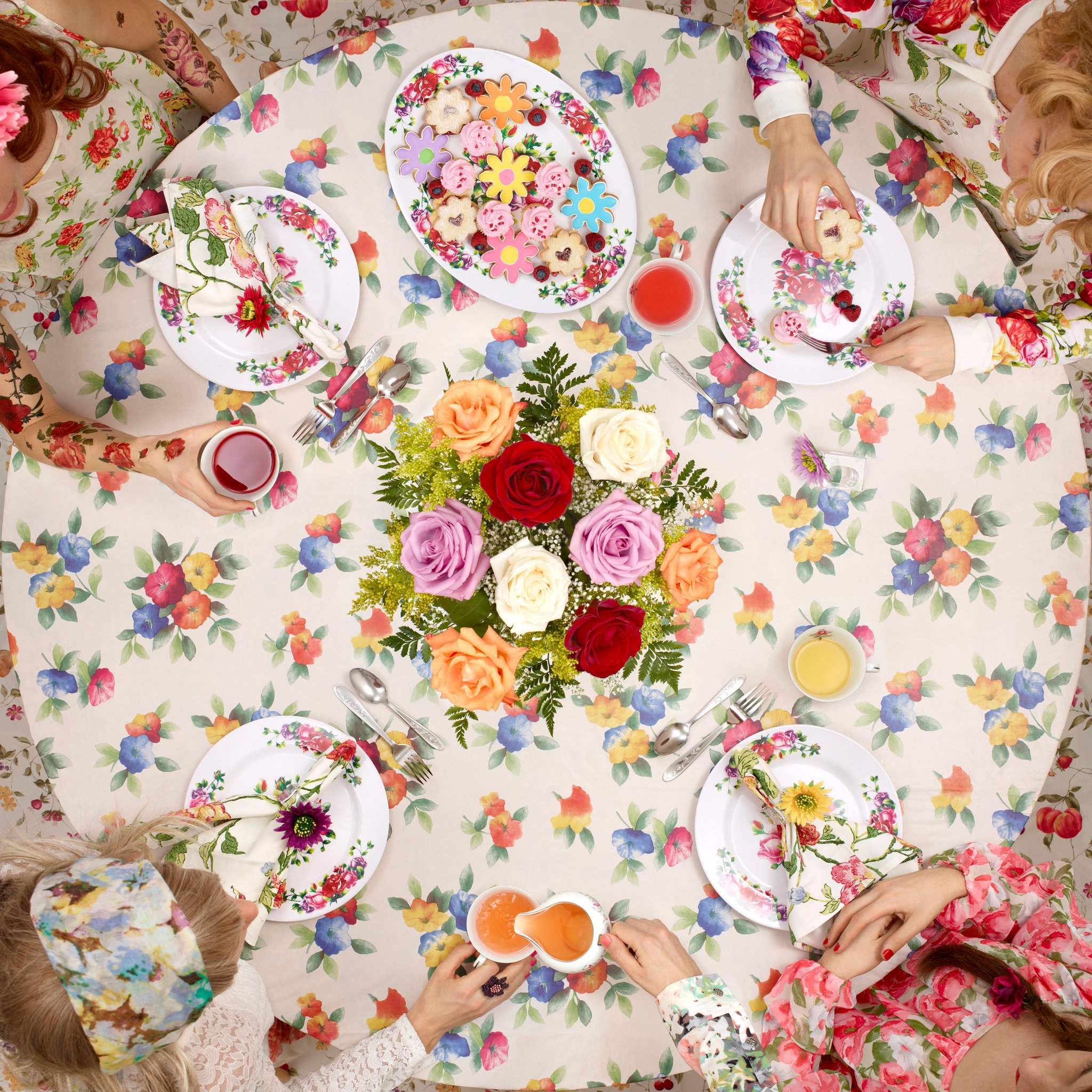 a group of young girls host tea time around a floral tablecloth