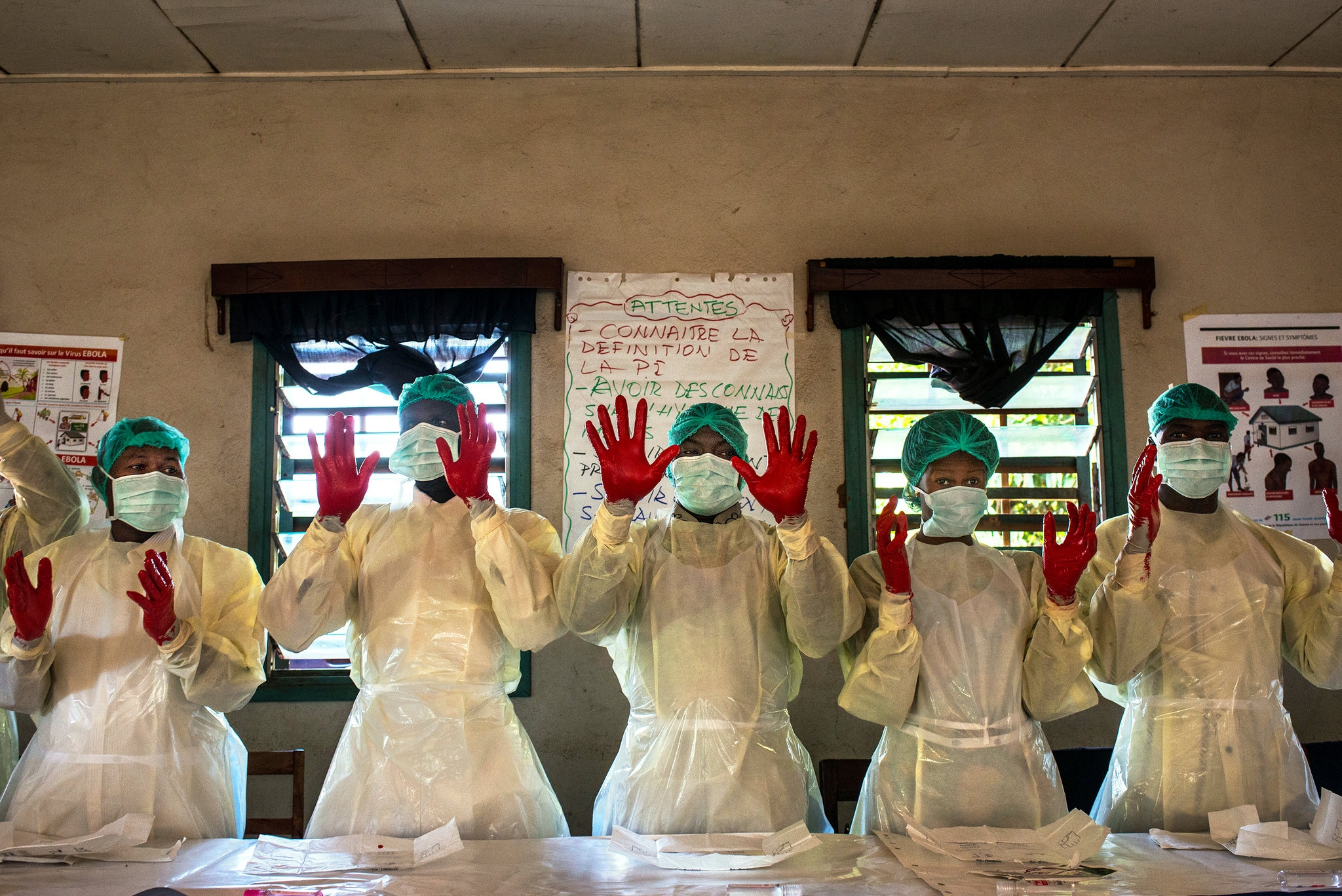 Students at an infection-prevention class showing their results in a hand-washing exercise while wrapped securely in medical robes, masks, and gloves