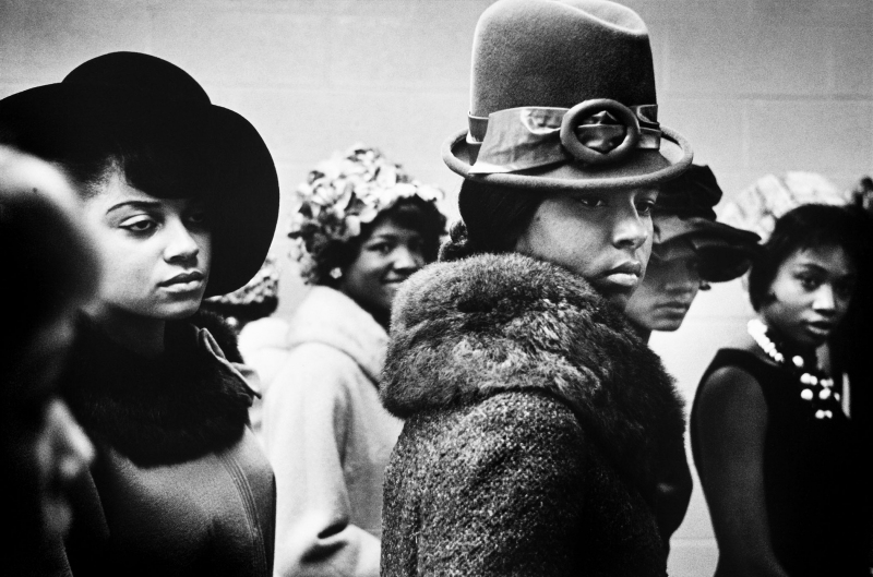 Several black women dressed in high fashion walk the runway