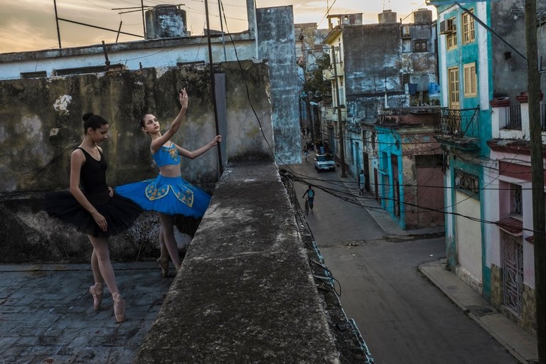 Two girls in ballerina attire practice on a Havana rooftop