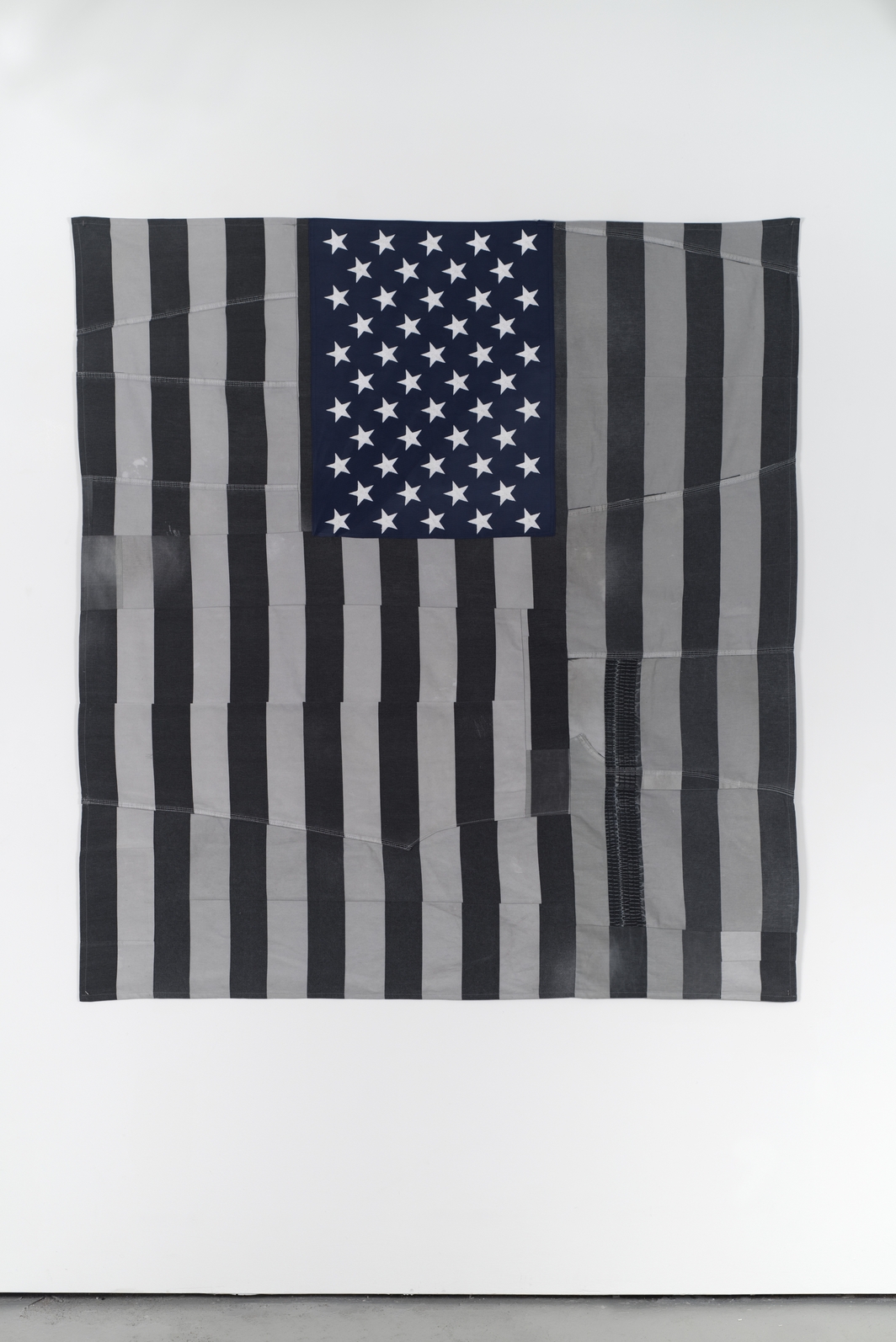 An American flag hangs on a wall that is made of striped prison uniforms