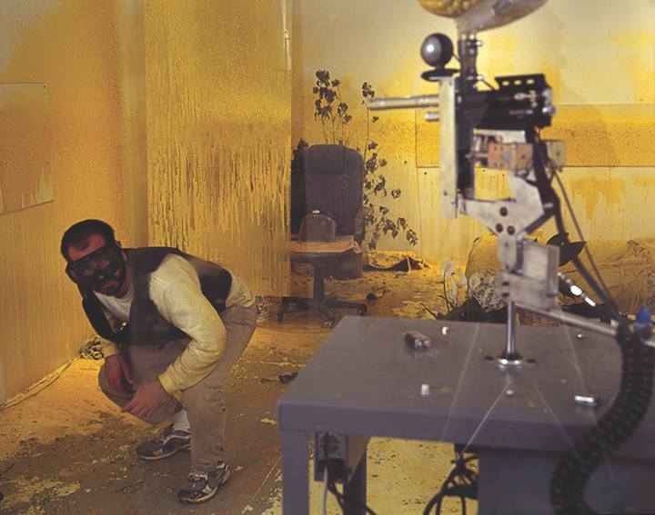 A man in tactical gear dodges shots from a paint gun in a small room