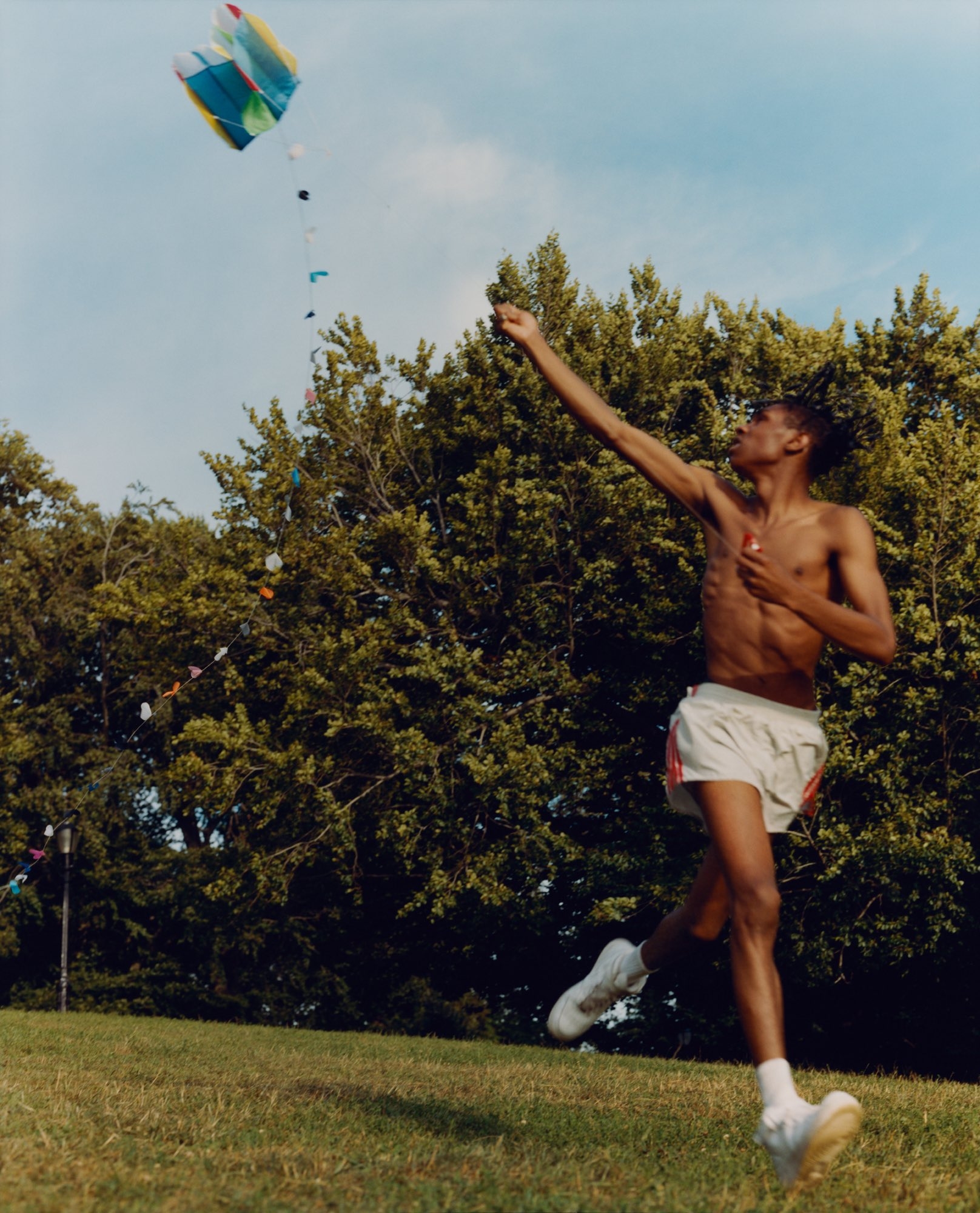 Color photo of an adolescent boy mid-leap with a kite in a field