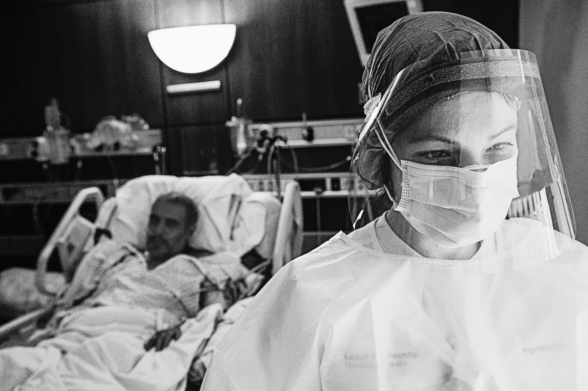 a black and white photo of a nurse in a face shield standing before a man in a hospital bed