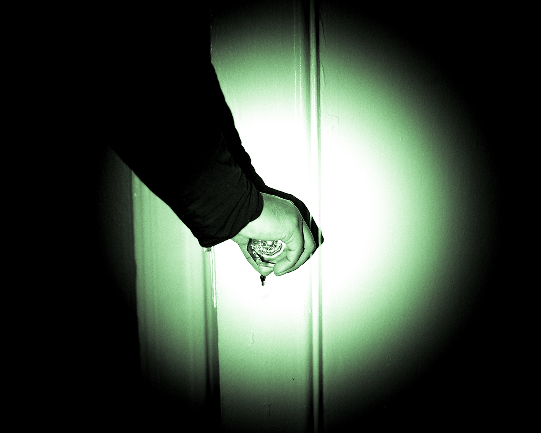 A spotlight shines on a close up of a hand gripping a door handle