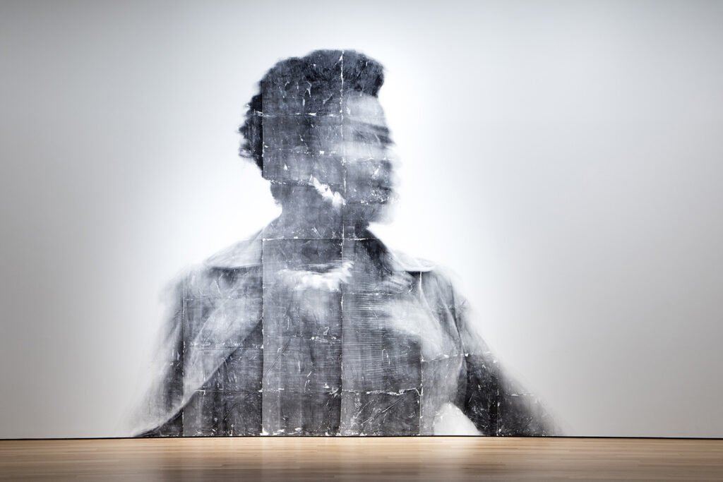 installation view of a larger than human scale portrait of a person in blurred focus