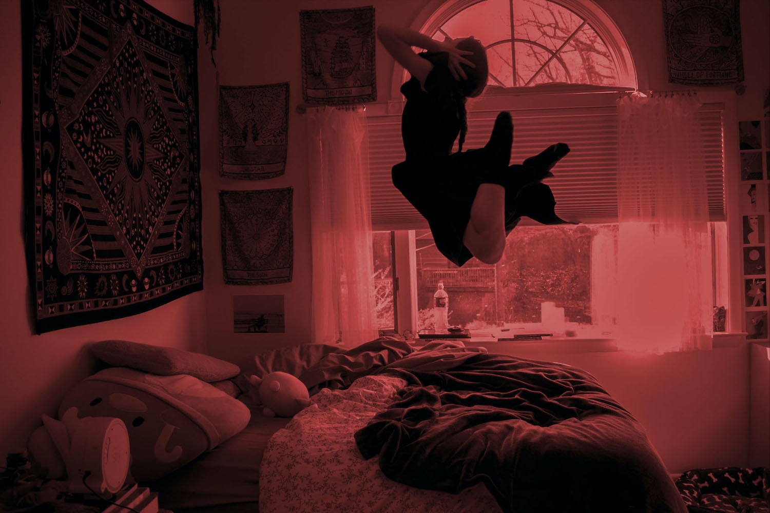red toned black and white with person jumping in the air of their bedroom
