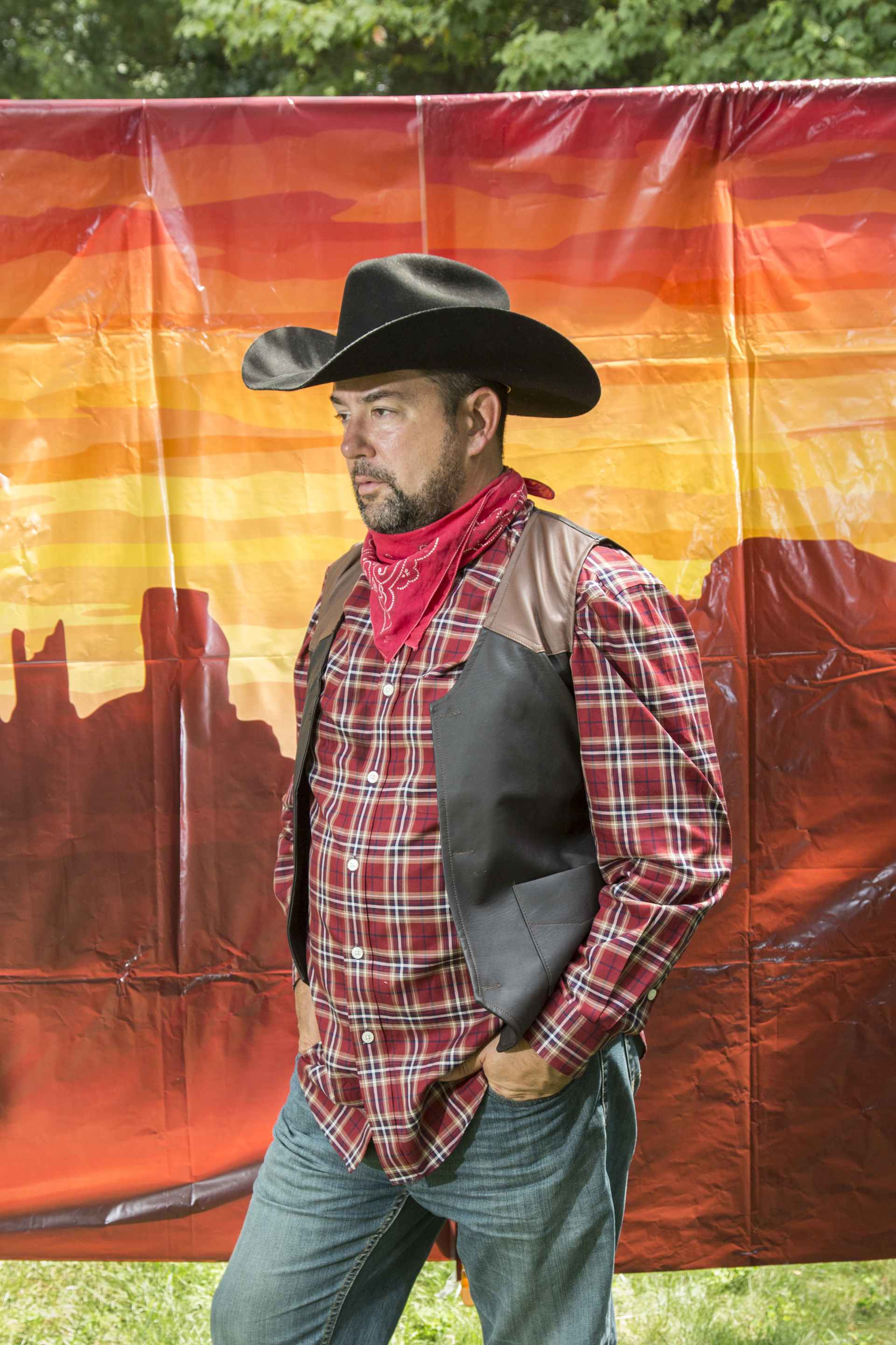 middle aged man in cowboy costume with faux western background