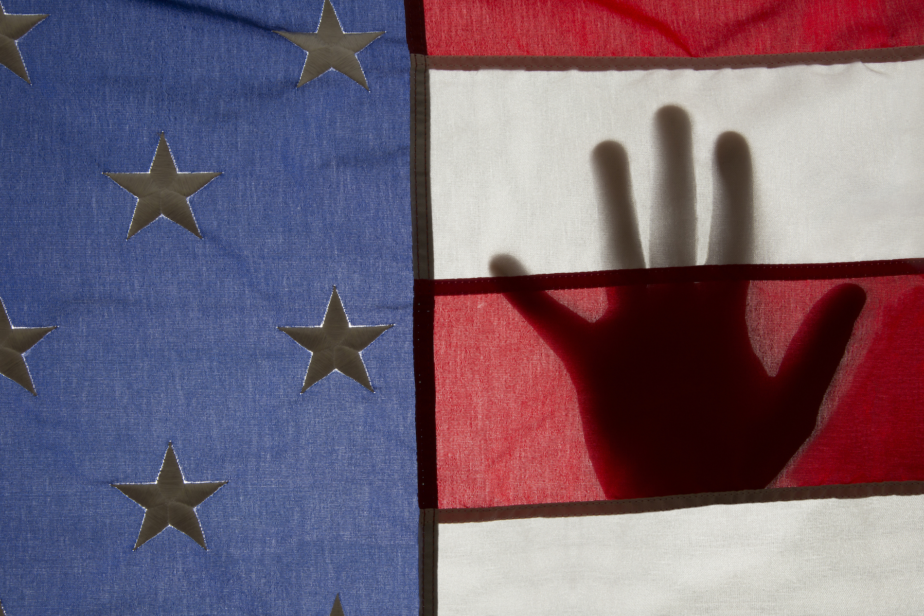 Color photo of a hand silhouetted behind an American flag by Chester Higgins