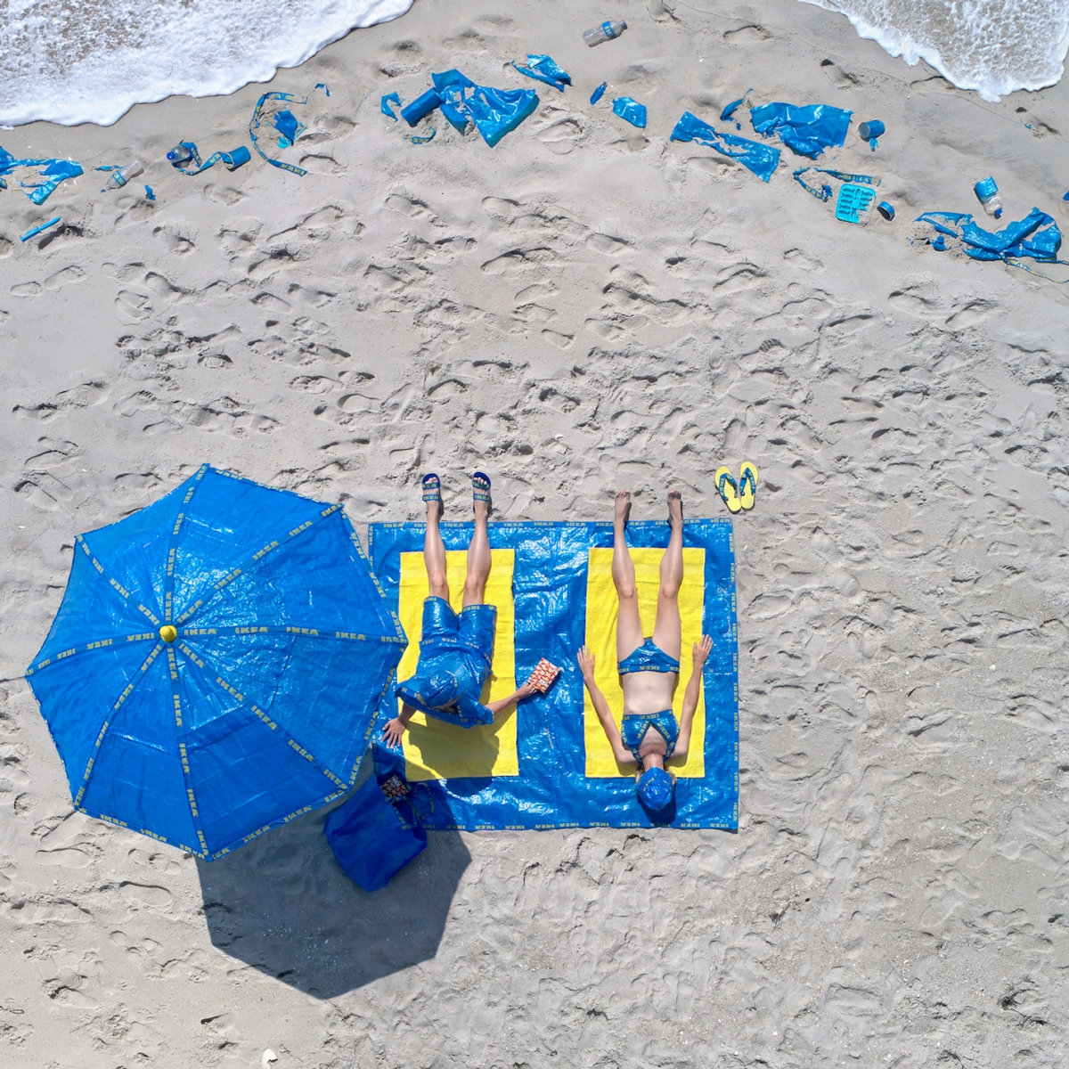 Photograph of a couple sunbathing using towels, beach umbrella, bathing suits and other items made of IKEA plastic bags.