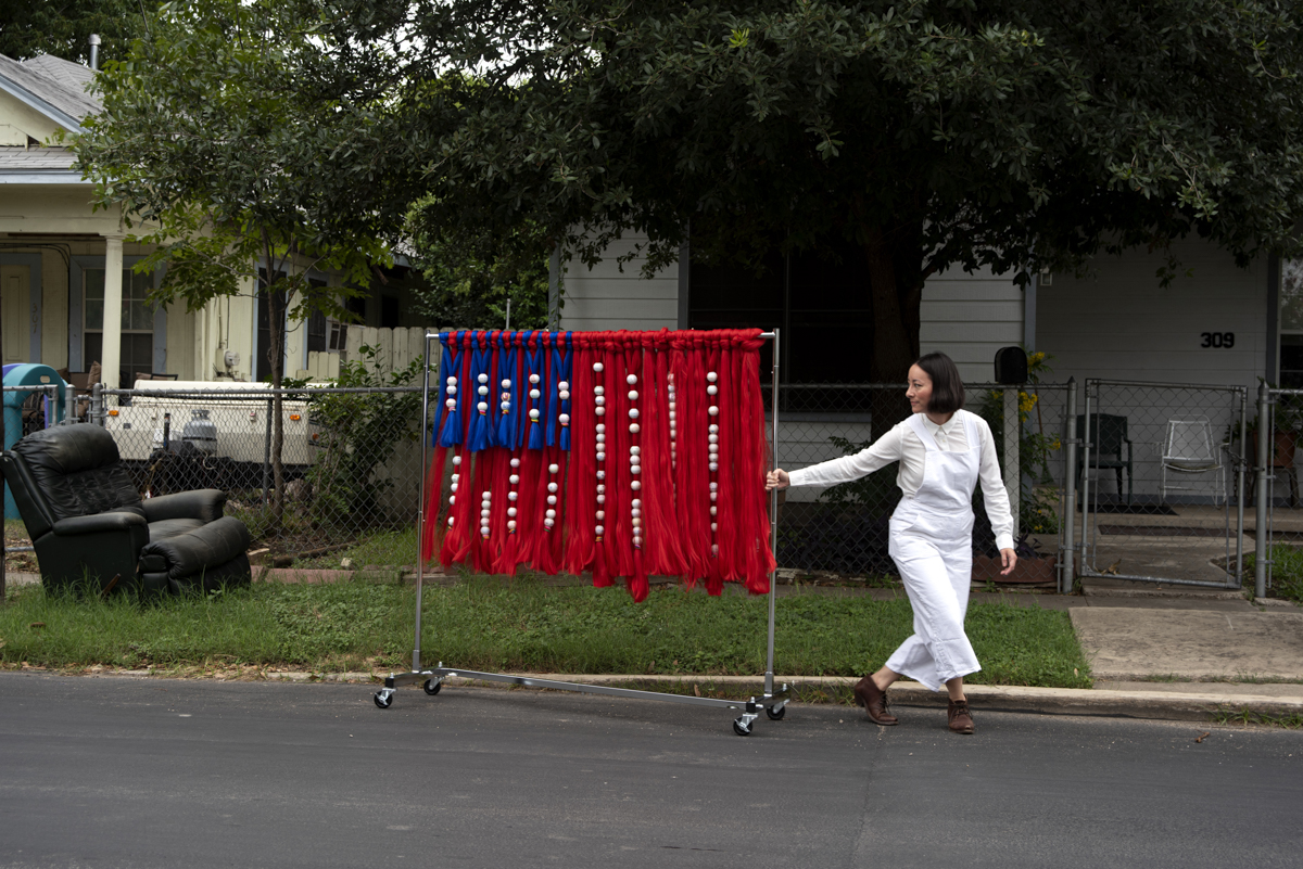 woman rolling art installation down of fabricated US flag down the street