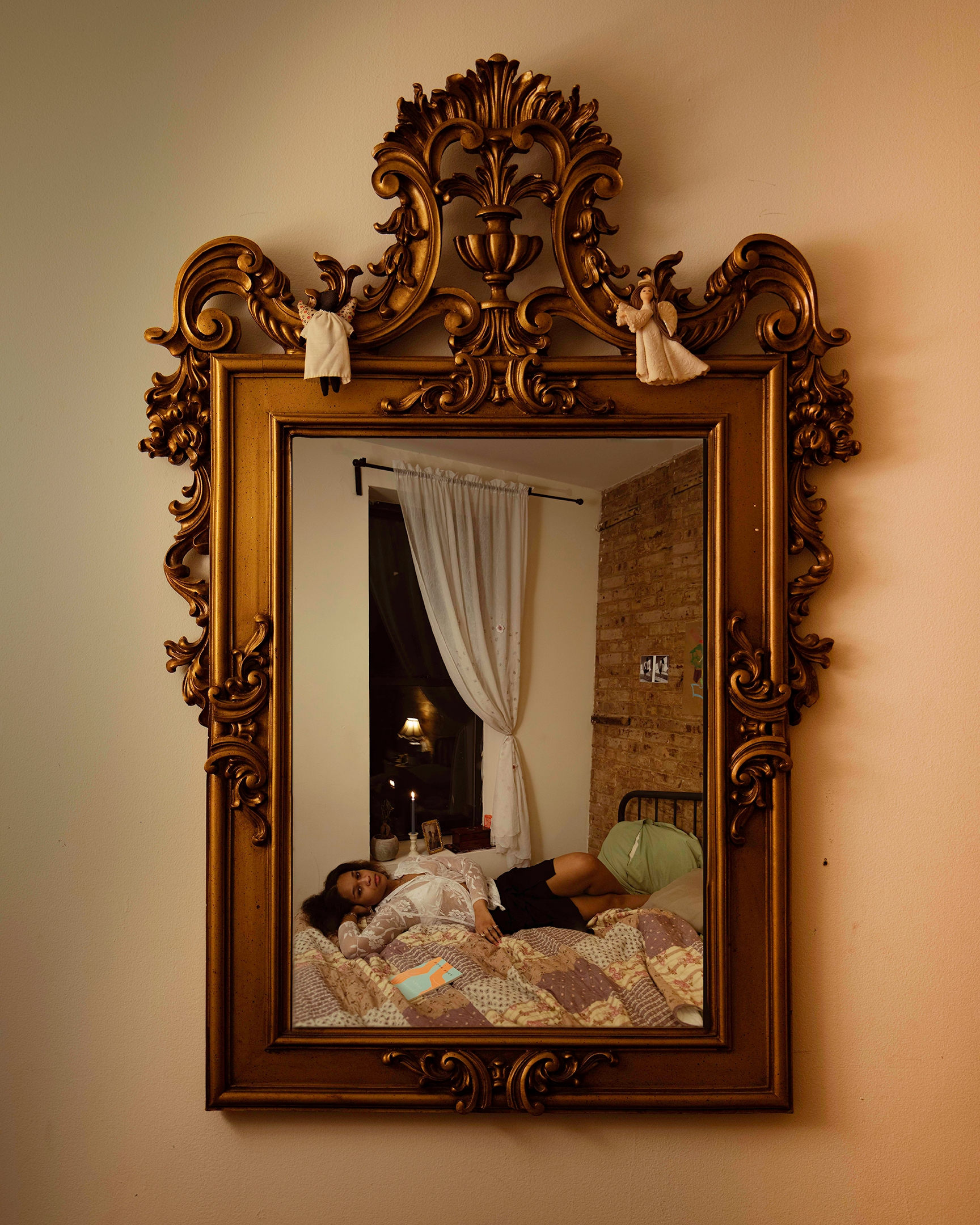 Gold mirror reflecting a girl laying across a bed in front of a window