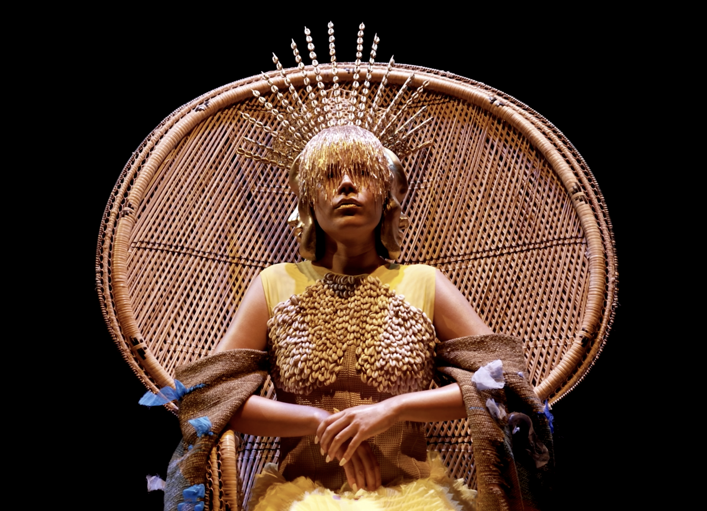 Image of a woman wearing a gold grown and dress seated at a wooden thrown