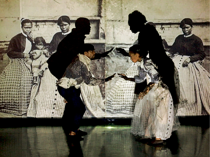 Two dancers on a stage posing. There is a black and white images projected on the dancers