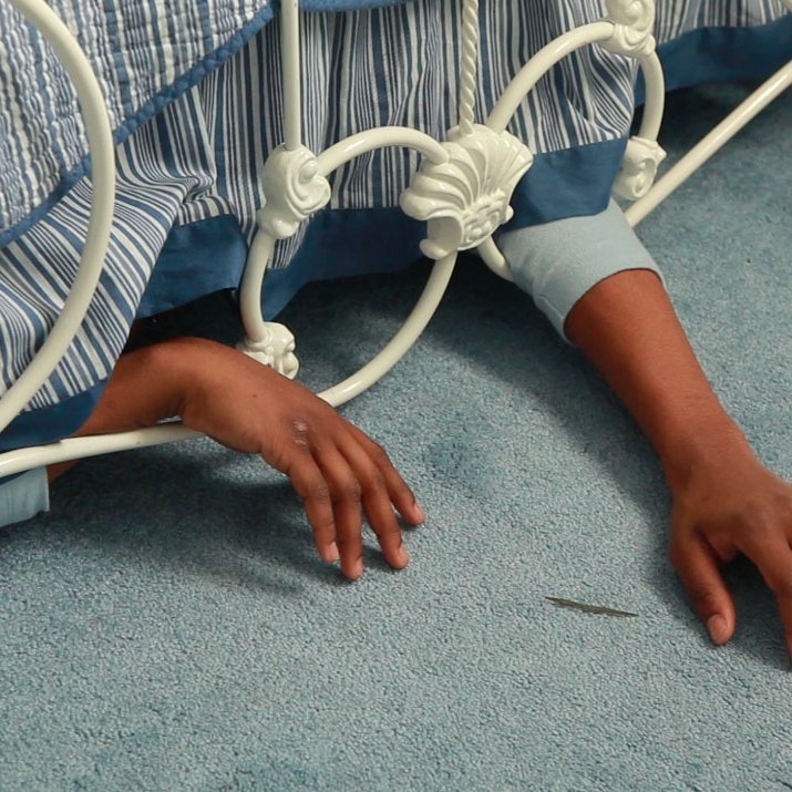Portrait of person under a bed with arms exposed, by Elliot Brown, Jr.